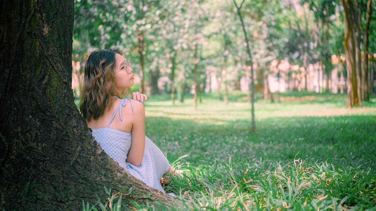 A woman sits by a tree in a peaceful park.